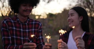 hermosa mujer asiática y novio sosteniendo fuegos artificiales quemando bengalas jugando en el festival de año nuevo, vestidos con camisa a cuadros, saludando con las manos, se ríen y disfrutan en la noche de fiesta de año nuevo video