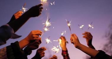 Selective focus, Close up group of hands holding fire burning sparklers and raising on sky in New year party video