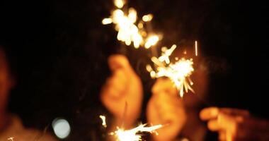 toma de mano, grupo borroso de adolescentes sosteniendo y disfrutando jugando con fuegos artificiales quemando bengalas en la noche de fiesta de año nuevo al aire libre video