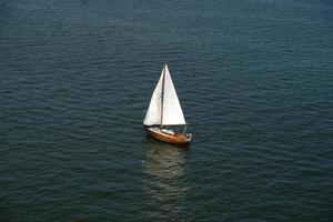 Aerial view of wooden old yacht with sail against backdrop of blue water with waves and ripples. Lonely white sail is sailing. Perfect content for posters or advertising banners, creative projects. photo