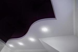 Detail of corner ceiling with intricate stucco work. Suspended ceiling and drywall with halogen spots lamps in room in apartment or house. Stretch purple ceiling of complex shape. photo