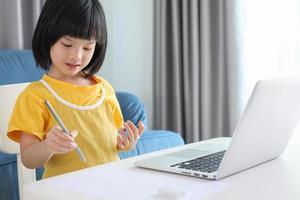 little asian girl student study online using laptop computer at home photo