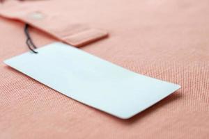 Blank white clothes tag label on pink fabric texture background photo
