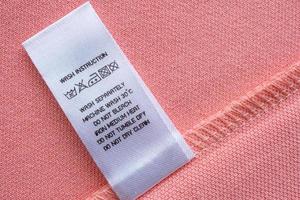 White laundry care washing instructions clothes label on pink cotton shirt photo