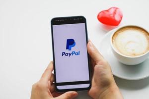 chiang mai, tailandia - 23 de agosto de 2020 - mujer usa un teléfono inteligente en la mesa que muestra páginas web de paypal en pantalla. es un método popular e internacional de transferencia de dinero a través de Internet. foto