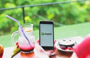 chiang mai, tailandia - 11 de julio de 2020 - una mujer sostiene un teléfono móvil iphone 7 plus con aplicación shopify en la pantalla en una panadería y cafetería. Shopify es una plataforma de comercio electrónico para tiendas en línea. foto