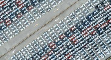 Aerial view of new cars stock at factory parking lot. Above view many cars parked in a row. Automotive industry. Logistics and supply chain business. Import or export new cars at warehouse near port. photo