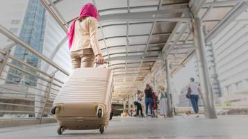mujer viajera musulmana caminando y llevando una maleta en un lugar de viaje en vacaciones o viaje de negocios, conceptos de viaje, vista trasera.