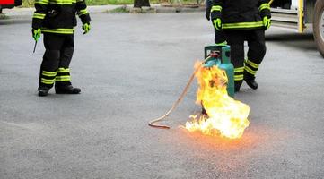 fuego ardiendo en un contenedor de gas verde y dos bomberos o bomberos con uniforme de seguridad negro y verde o traje y extinguir el fuego en la calle con fondo de rueda de camión y espacio para copiar. conflagración. foto