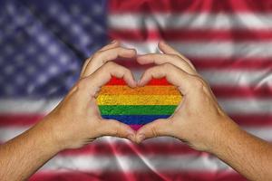 male hands forming a heart with an LGBT flag inside against the background of the USA flag photo