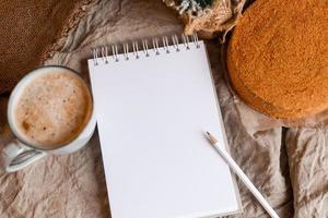 a notebook with empty pages on a wooden table with coffee and homemade honey cake. A notebook for recipes, cooking at home. Homemade cakes, space for text