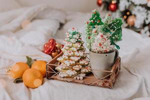 Christmas sweets, gingerbread painted with icing, lollipops and meringues in the shape of Christmas trees and tangerines on a beautiful tray. homemade cakes. delicious food for the winter holidays photo