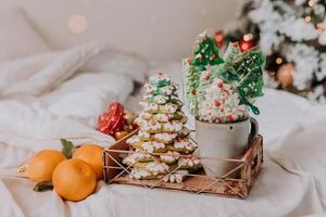 dulces navideños, pan de jengibre pintado con glaseado, piruletas y merengues en forma de árboles de navidad y mandarinas en una bonita bandeja. tortas caseras deliciosa comida para las vacaciones de invierno foto