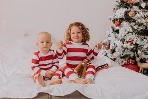 los niños en pijama rojo y blanco prueban gafas divertidas con santa claus sentado en la cama. estilo de vida. hermano y hermana celebrando la navidad. niño y niña están jugando en casa. foto de alta calidad