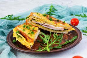 Roasted toast in scrambled eggs with ham, herbs and cheese cheddar. Delicious grilled breakfast sandwich photo