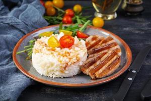 Rice with grilled pork meat, tomatoes and green herbs on dark background