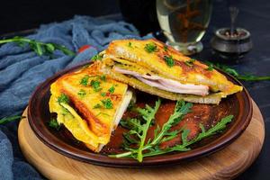Roasted toast in scrambled eggs with ham, herbs and cheese cheddar. Delicious grilled breakfast sandwich photo