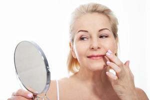 Happy middle aged woman model touching face skin looking in mirror. Smiling mature older lady enjoying healthy skin care, aging beauty, skincare treatment cosmetic products concept. photo