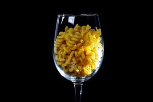 raw pasta in glass jar, wine glass. in bucket. raw pasta on black background. front view raw pasta, dropped from hand, place for text, yellow long spaghetti straws, photo