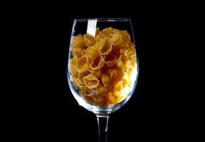 raw pasta in glass jar, wine glass. in bucket. raw pasta on black background. front view raw pasta, dropped from hand, place for text, yellow long spaghetti straws, photo