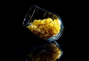 raw pasta in glass jar, wine glass. in bucket. raw pasta on black background. front view raw pasta, dropped from hand, place for text, yellow long spaghetti straws, photo