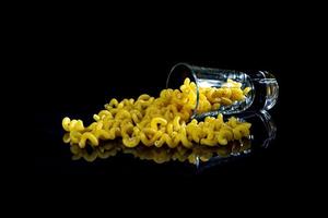 raw pasta in glass jar, wine glass. in bucket. raw pasta on black background. front view raw pasta, dropped from hand, place for text, yellow long spaghetti straws, photo