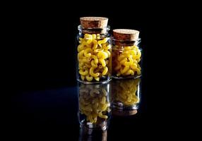 raw pasta in glass jar, wine glass. in bucket. raw pasta on black background. front view raw pasta, dropped from hand, place for text, yellow long spaghetti straws, photo