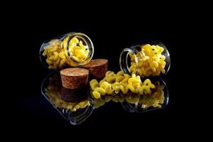 raw pasta in glass jar, wine glass. in bucket. raw pasta on black background. front view raw pasta, dropped from hand, place for text, yellow long spaghetti straws, photo