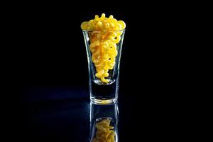 raw pasta in glass jar, wine glass. in bucket. raw pasta on black background. front view raw pasta, dropped from hand, place for text, yellow long spaghetti straws, photo