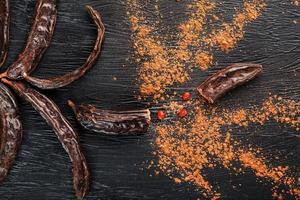 Carob fruit on a black textured background in the shape of an exploding flower. photo