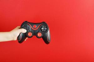 A child's hand holds a gamepad on a red background. Free space, minimalistic creative concept of the Younger generation of gamers. photo