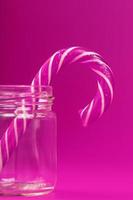 One Lollipop Candy cane in a glass jar on a pink background. photo