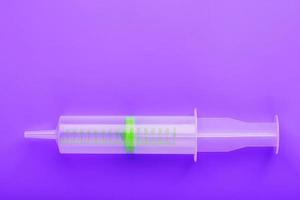 Green medical syringe on crazy lilac background. The concept of minimalism and free space.