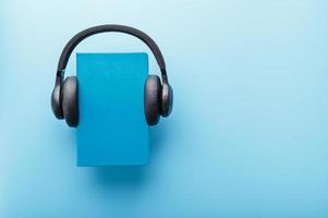 Headphones are worn on a book in a blue hardcover on a blue background, top view. photo