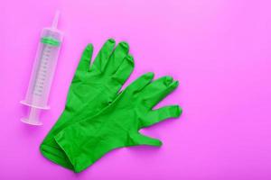 Green medical syringe and gloves on crazy lilac background. photo