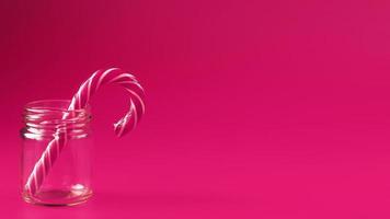 One Lollipop Candy cane in a glass jar on a pink background. photo