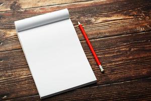 Notepad with red pencil on a brown wooden table background, for education, write goals and deeds photo