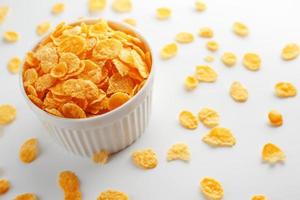 White cup with golden corn flakes, isolated on white background. Hopya crumbled around the cup. View from above photo