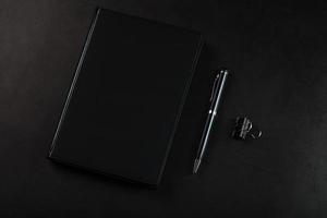 escritorio de oficina con bloc de notas negro y bolígrafo sobre fondo negro. foto