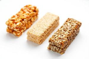 barra de granola de grano con cacahuetes, sésamo y semillas seguidas sobre un fondo blanco. vista superior tres barras variadas, aislar foto