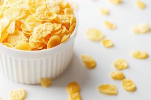 White cup with golden corn flakes, isolated on white background. Hopya crumbled around the cup. View from above photo