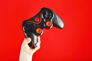 A child's hand triumphantly holds the gamepad on a red background. photo
