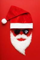 Santa Claus Hat and beard made of snow with black glasses on red background. photo