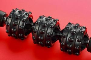Black lumpy foam body massage roller on red background. photo