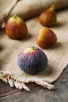 higos orgánicos maduros sobre la mesa. grupo de higos morados y verdes en una mesa de madera de granja con tela de arpillera foto