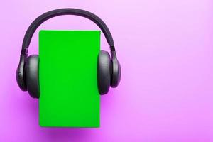 Headphones are worn on a book in a green hardcover on a lilac background, top view. photo