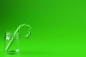 un bastón de caramelo de piruleta en un frasco de vidrio sobre un fondo verde. foto