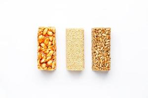 Grain granola bar with peanuts, sesame and seeds in a row on a white background. Top view Three assorted bars, isolate photo