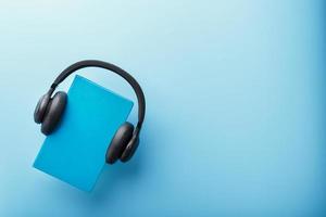 los auriculares se usan en un libro de tapa dura azul sobre un fondo azul, vista superior. foto