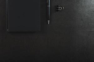 escritorio de oficina con bloc de notas negro y bolígrafo sobre fondo negro. foto